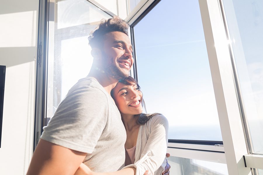 Personal Insurance - Smiling Couple Looking Out Window of Luxury Condo on a Bright Sunny Day