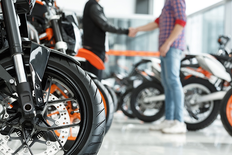 Motorcycle Dealership Insurance - Focus-on a Motorcycle Wheel with Male Customer Shaking Hands with Motorcycle Dealership Manager in the Background